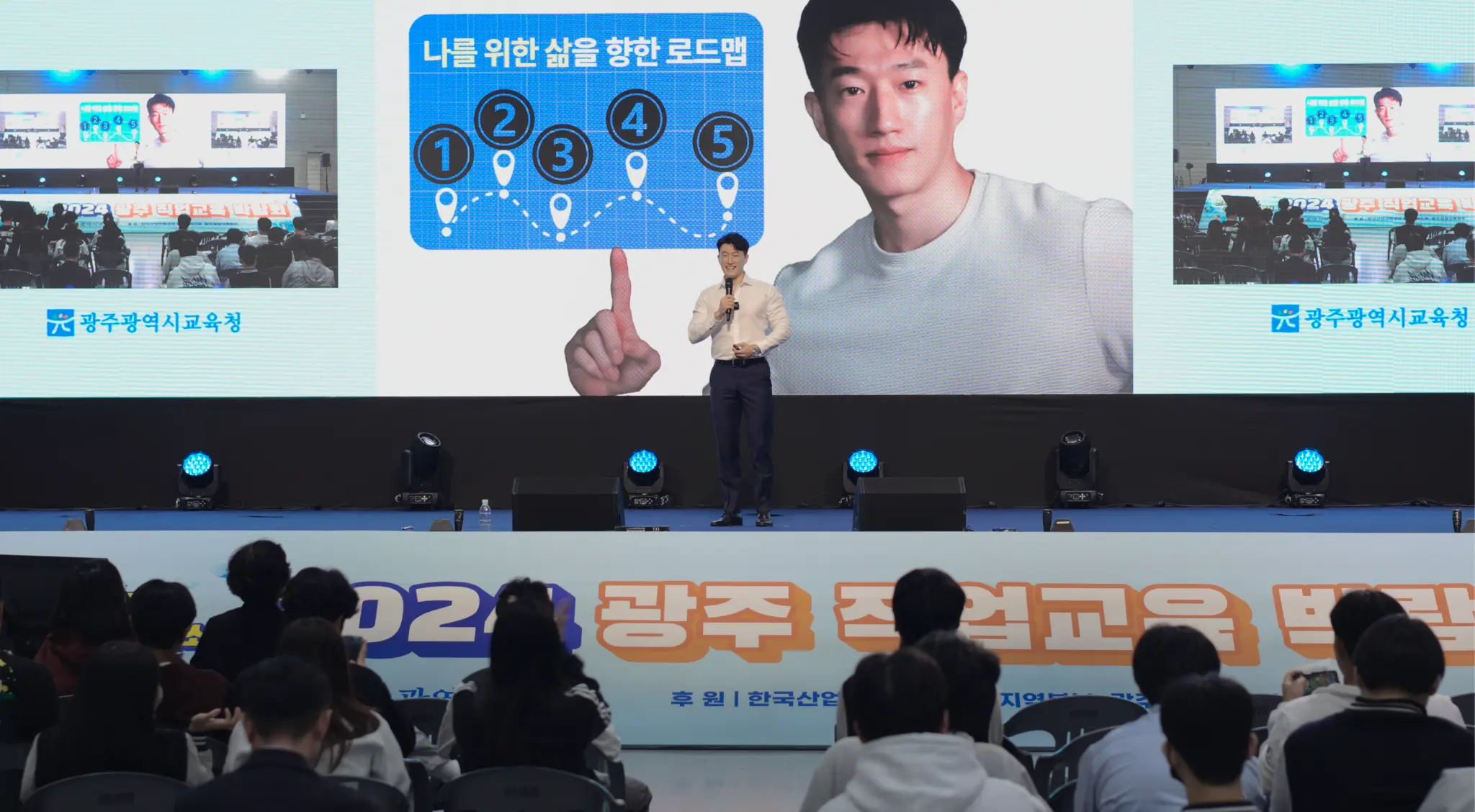 Youngjin Koh speaking on stage to hundreds of students